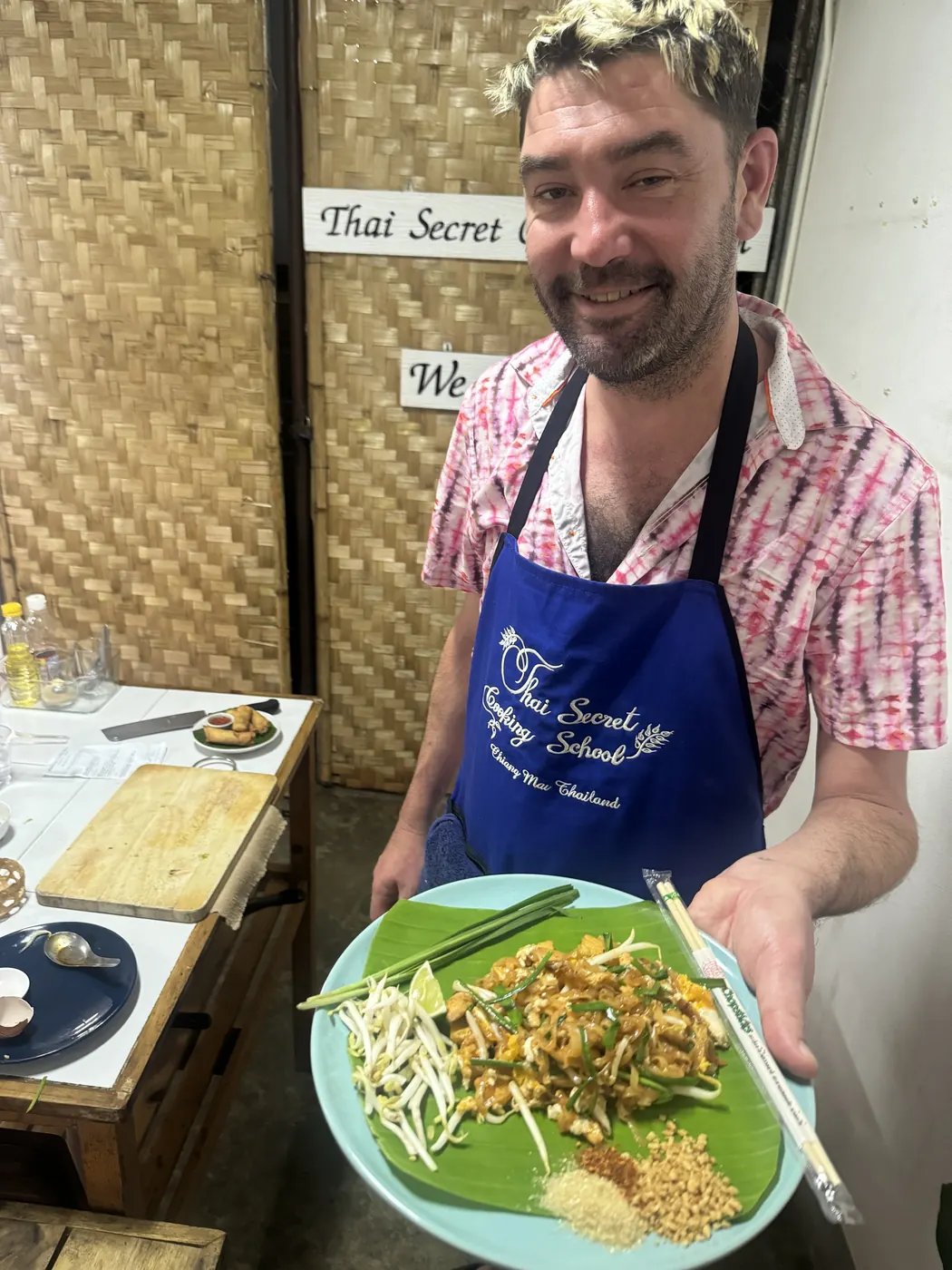 Christopher holding up a banana leaf plate of pad thai with bean sprouts, lime and crushed peanuts at the Thai Secret Cooking School.